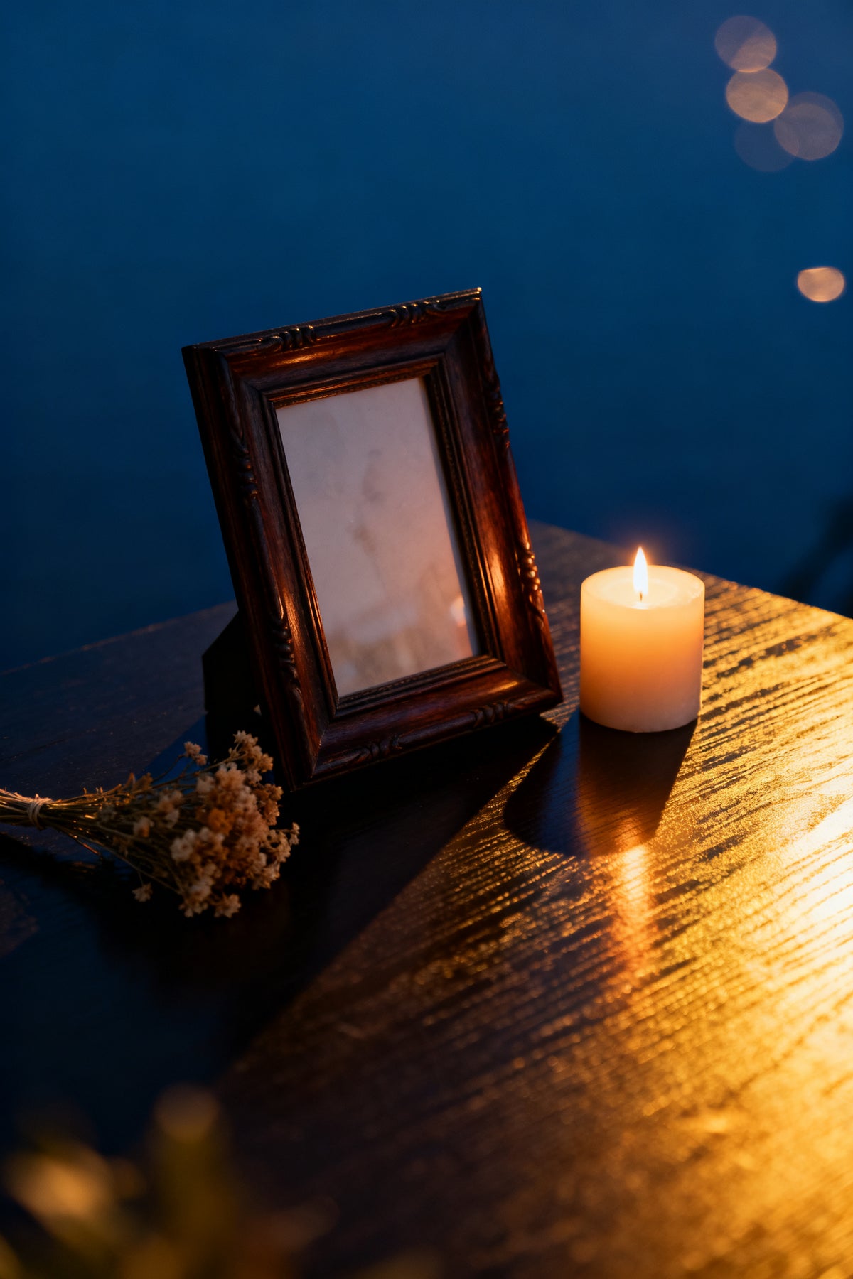 Hommage personnalisé — cadre photo ancien, bougie allumée et fleurs séchées dans une lumière dorée douce